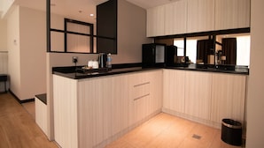 A modern kitchen with light wood cabinets, a black countertop, and a built-in microwave. - Higher Hotel (Bandar Seri Begawan)