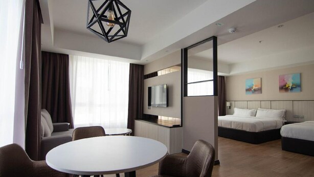 A modern hotel room with a round dining table, two sofas, a TV, a bed, and artwork on the wall. - Higher Hotel (Bandar Seri Begawan)