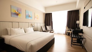 A modern hotel room with a large bed, two armchairs, a desk, and artwork on the walls. - Higher Hotel (Bandar Seri Begawan)