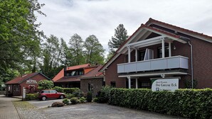 Un hotel con un coche rojo estacionado frente, un letrero que indica 'Hotel Pension Dat Greune Eck' y un camino pavimentado que conduce a la entrada.