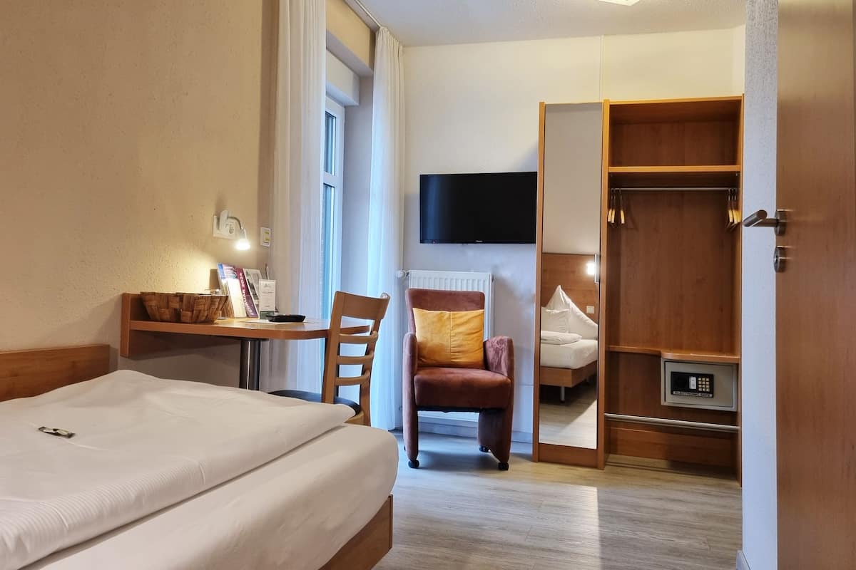 Una habitación de hotel con cama, escritorio y silla, televisión montada en la pared y armario.