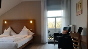Una habitación de hotel con cama, escritorio, silla y ventana con cortinas.