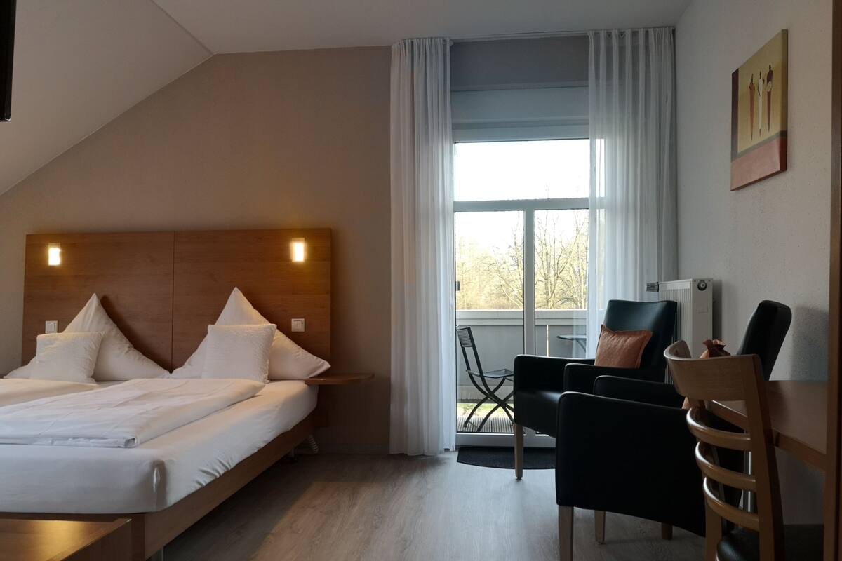 Una habitación de hotel con cama, escritorio, silla y ventana con cortinas.