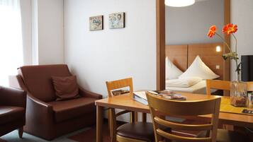 Et hotelværelse med en brun lædersofa, et træspisebord med to stole, en seng med hvidt sengetøj og to billeder på væggene.