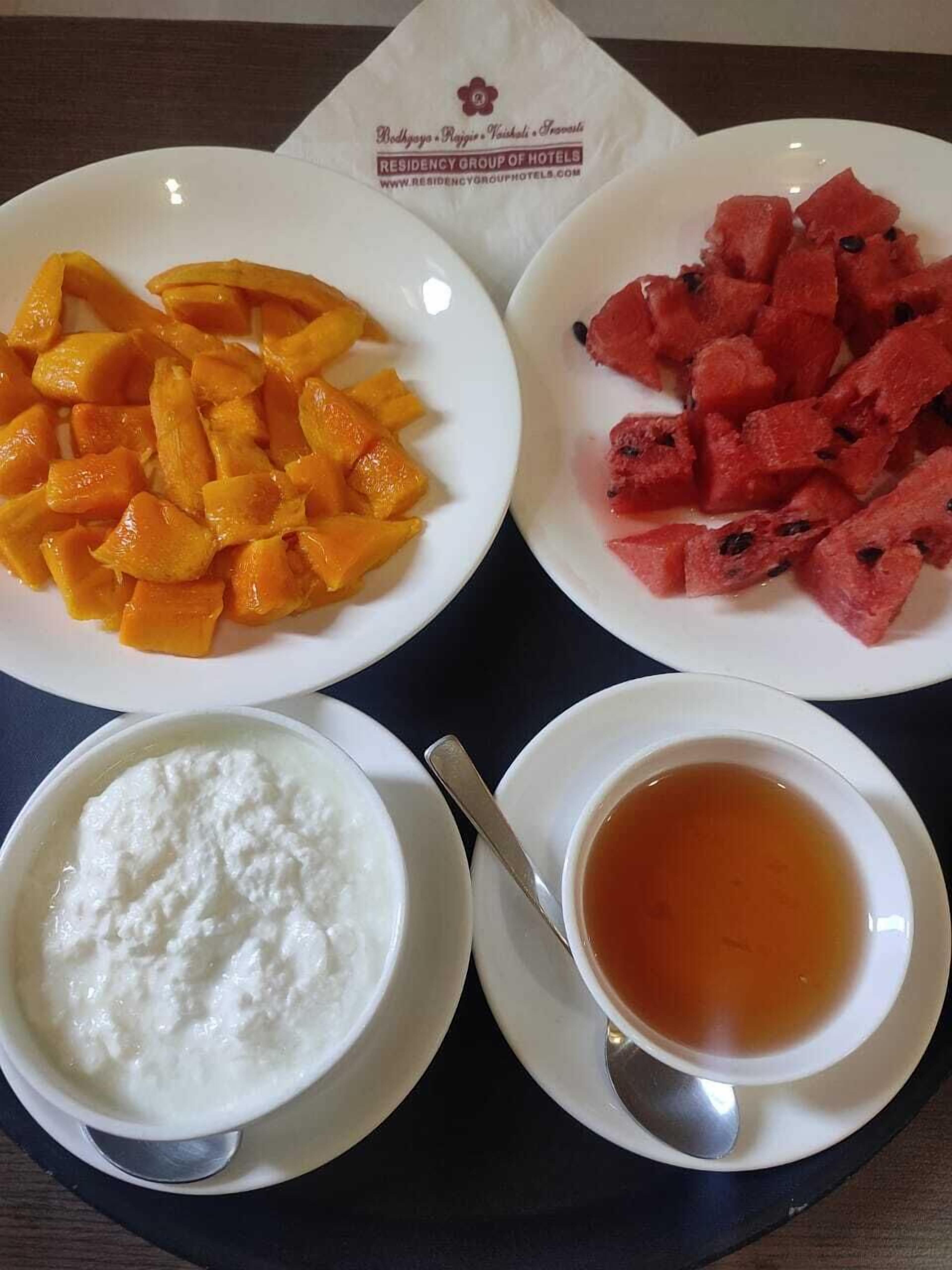 Una bandeja con trozos de mango, sandía, yogur y té.