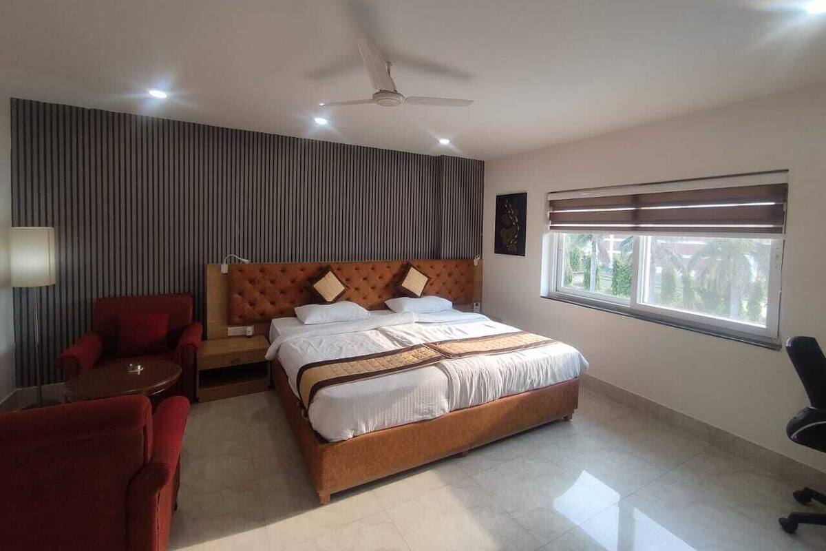 Une chambre à coucher moderne avec un grand lit, un ventilateur de plafond, une fenêtre avec des stores et un fauteuil rouge.