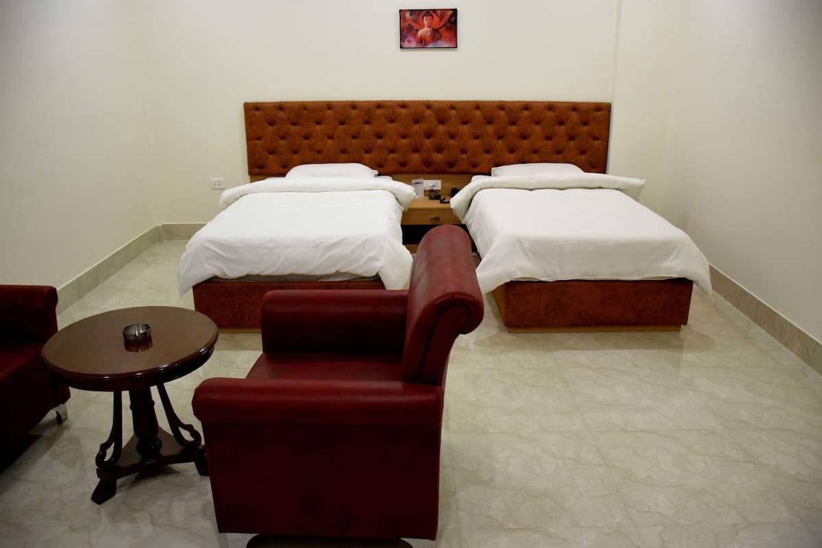 Une chambre d’hôtel avec deux lits simples, une tête de lit en bois, une petite table ronde et un fauteuil rouge.