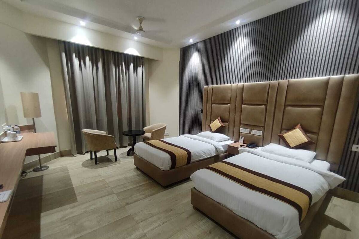 Une chambre d’hôtel avec deux lits, un bureau, une chaise et une grande fenêtre avec des rideaux.