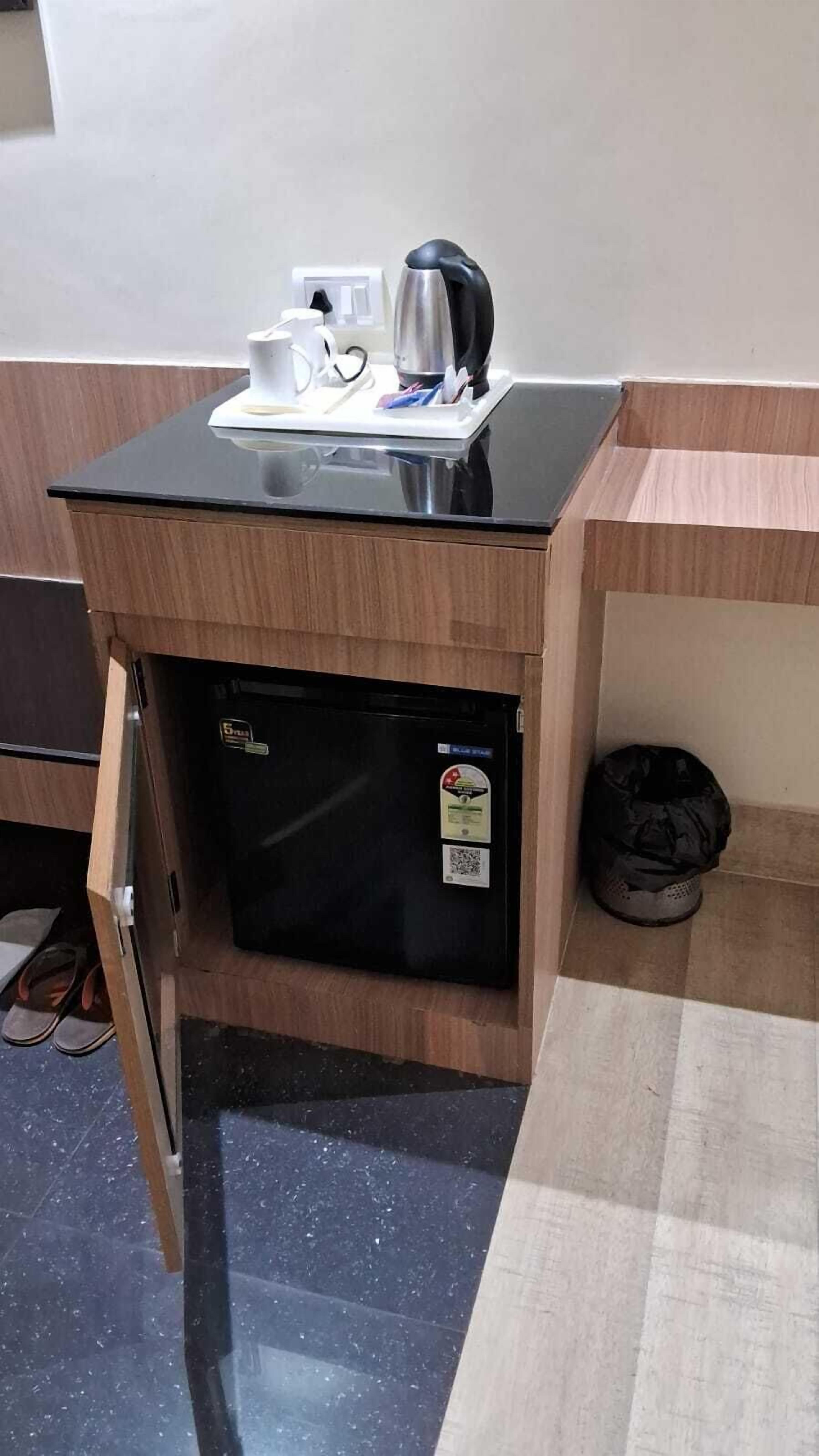 Pieni, käytännöllinen keittokomero, jossa on musta työtaso, pieni jääkaappi ja kahvinkeitin.