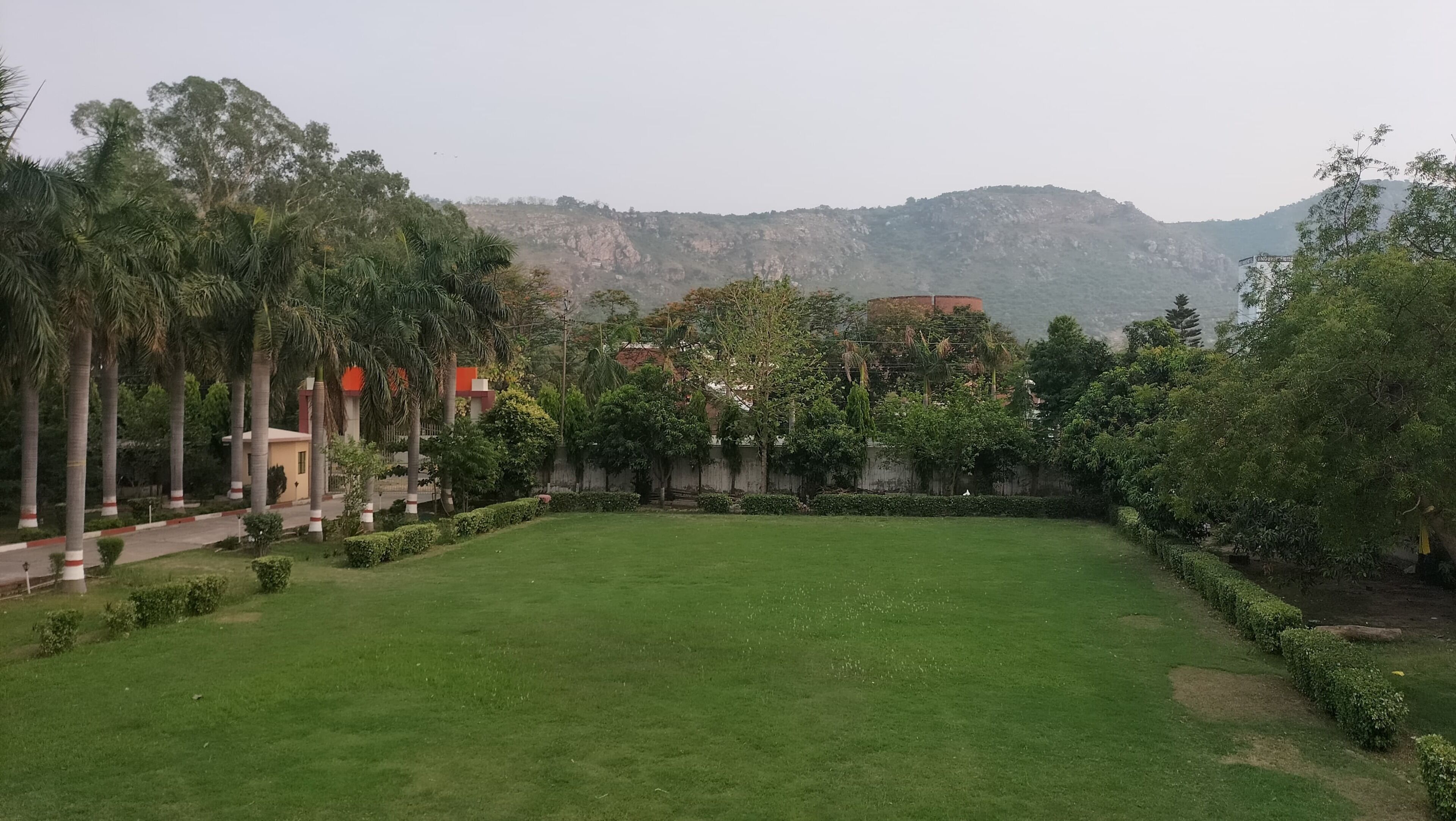 A well-maintained lawn with a pathway leading to a building, surrounded by trees and a mountain backdrop.