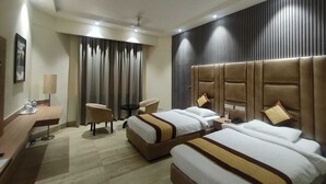 Habitación de hotel con dos camas, un escritorio, una silla y un ventanal grande con cortinas.