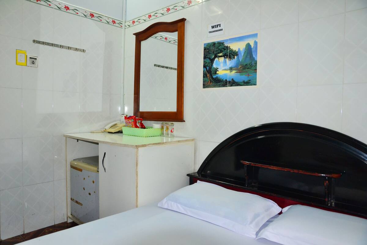 Une chambre d’hôtel comprenant un lit, un petit bureau avec un téléphone, un miroir, un tableau accroché au mur et un panneau indiquant la disponibilité du Wi-Fi.