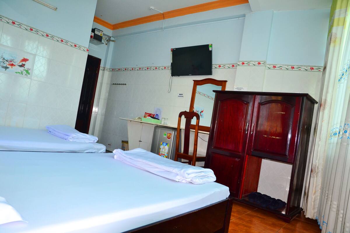 Une chambre d’hôtel avec deux lits, un téléviseur fixé au mur, une armoire en bois et un petit bureau avec un réfrigérateur.