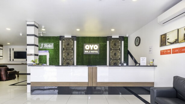 A hotel reception area with a modern design, including a reception desk, a clock, and a seating area with a sofa. - OYO 718 MR J Hotel Wakaf Che Yeh 1 (Kota Bharu)