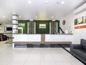 Un espace d’accueil d’hôtel au design moderne, comprenant un comptoir d’accueil, une horloge et un coin salon avec un canapé.