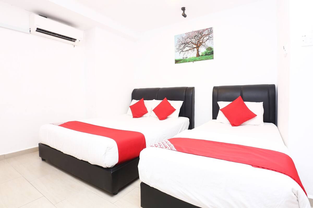 Une chambre d’hôtel avec deux lits, chacun doté d’un cadre noir et de draps blancs agrémentés d’oreillers rouges.