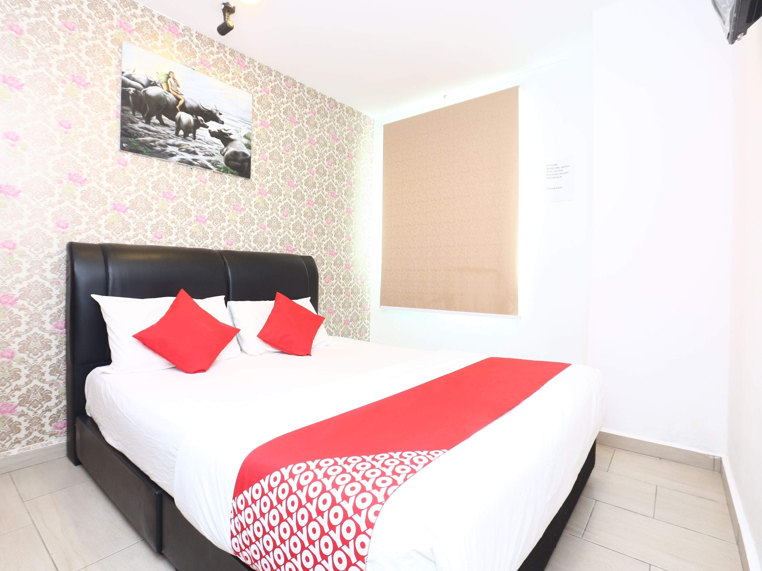 A neatly made bed with a white and red patterned bedspread, a black headboard, and red pillows.