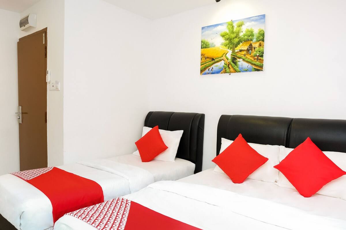 Une chambre d’hôtel avec deux lits, chacun recouvert d’une courtepointe rouge et blanche et agrémenté d’oreillers. Un tableau représentant un paysage est accroché au mur.
