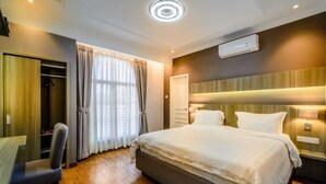A hotel room with a large bed, a desk with a chair, a wardrobe, and a window with curtains. - Villa Kota Bunga Puncak 2 Bedroom (Cipanas)