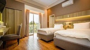 A hotel room with two beds, a desk, a chair, and a large window with curtains. - Villa Kota Bunga Puncak 2 Bedroom (Cipanas)