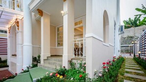 A hotel entrance with a covered porch, white columns, and a staircase leading to the entrance. - Villa Kota Bunga Puncak 2 Bedroom (Cipanas)