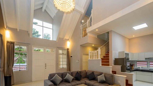 A spacious living area with a large sectional sofa, a staircase, and a kitchen area. - Villa Kota Bunga Puncak 2 Bedroom (Cipanas)