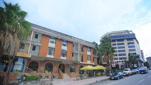 Et hotel med en moderne facade, flere balkoner og udendørs siddepladser med parasoller.