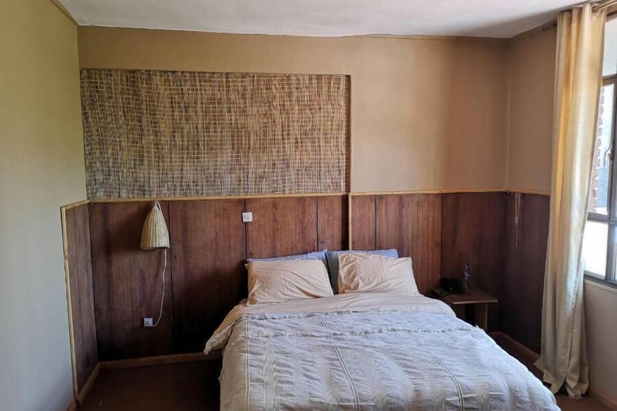 A single bed in a room with a wooden headboard, a small bedside table, and a window with curtains.