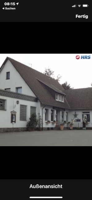 A building with a white facade and a sloped roof, featuring a small entrance with steps and potted plants. - Hotel Kämpgens - Hof (Muelheim an der Ruhr)
