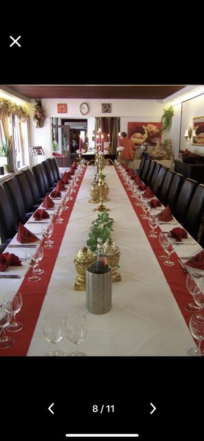 A long dining table with red napkins, wine glasses, and gold candle holders, set in a formal dining room with black chairs. - Hotel Kämpgens - Hof (Muelheim an der Ruhr)