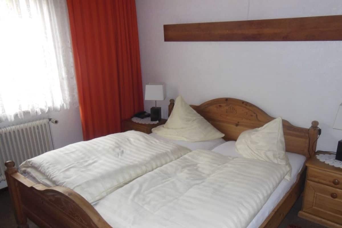 A double bed with a wooden headboard, a bedside table with a lamp, and a nightstand with a lamp.