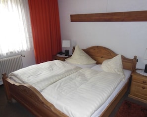 A double bed with a wooden headboard, a bedside table with a lamp, and a nightstand with a lamp. - Hotel Kämpgens - Hof (Muelheim an der Ruhr)
