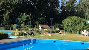 A swimming pool with a clear blue water surface, surrounded by greenery and a small building in the background. - Hotel Kämpgens - Hof (Muelheim an der Ruhr)