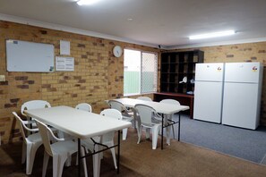 A room with a brick wall, white tables and chairs, a whiteboard, and a refrigerator. - Fantasy Ocean Holiday House (Coffs Harbour)