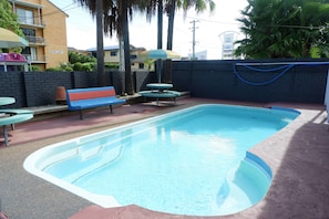 A swimming pool with a blue edge, a bench, and a table with an umbrella. - Fantasy Ocean Holiday House (Coffs Harbour)