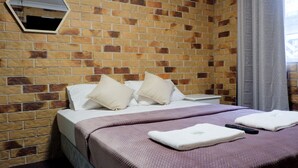 A hotel room with a brick-patterned wall, a bed with white linens and two pillows, a purple blanket, and two remote controls on the bed. - Fantasy Ocean Holiday House (Coffs Harbour)