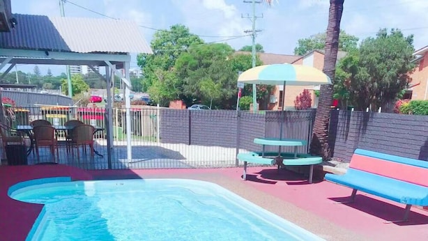 A swimming pool with a curved edge, surrounded by a fenced area with benches and a shaded seating area. - Fantasy Ocean Holiday House (Coffs Harbour)