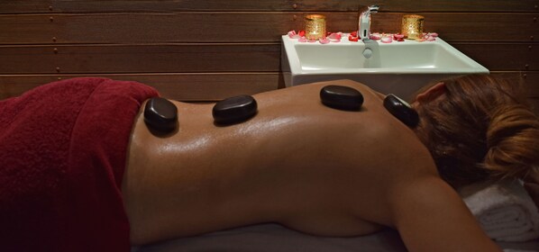 A person receiving a back massage with heated stones on a wooden floor.