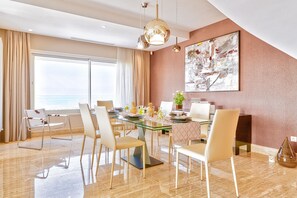 A modern dining area with a glass table, multiple chairs, and a view of the sea through large windows. - ADAM Hotel Suites (Tunis)