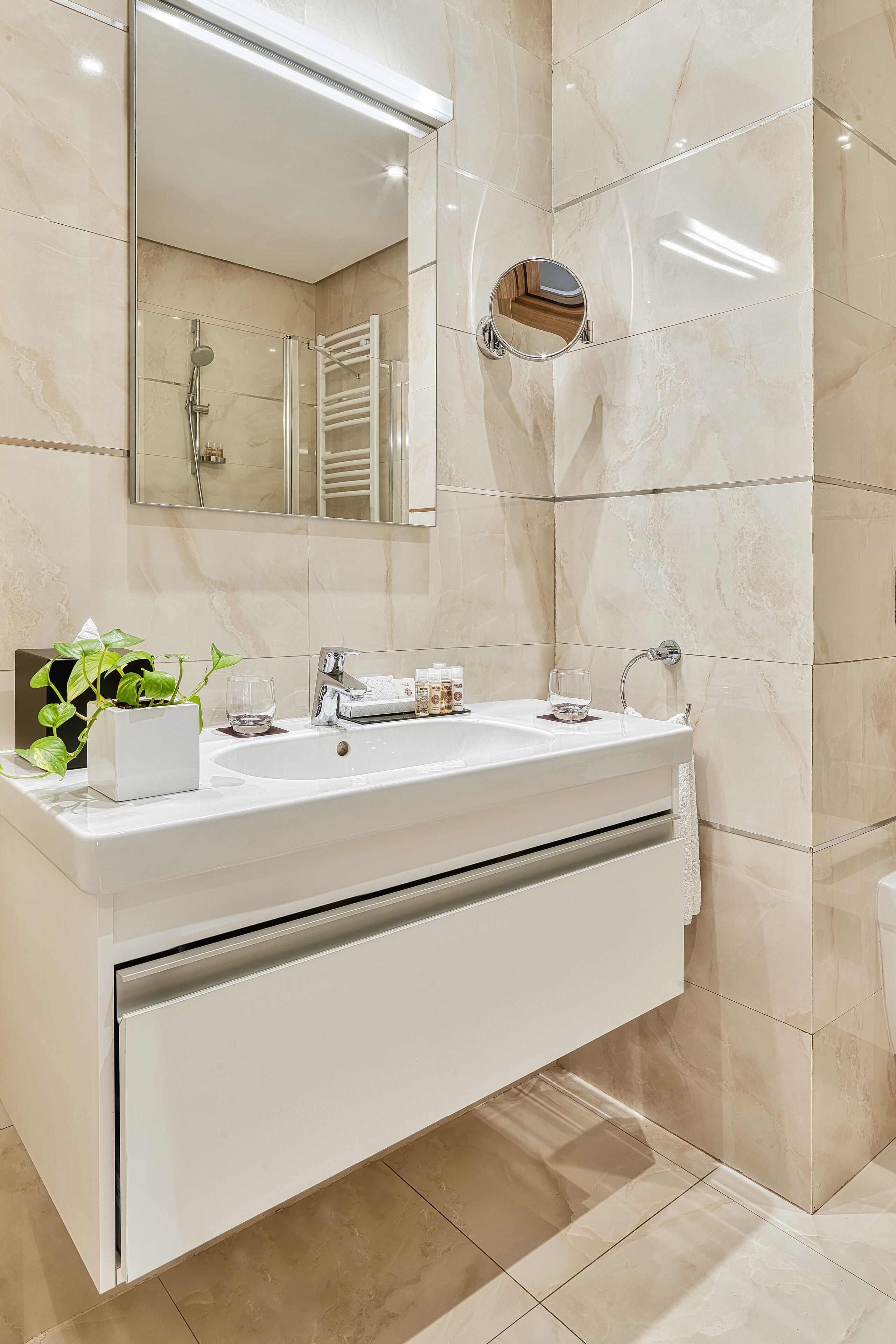 Un baño moderno con tocador blanco, un espejo grande y ducha con mampara de vidrio.