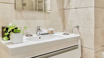 Un baño moderno con tocador blanco, un espejo grande y ducha con mampara de vidrio.