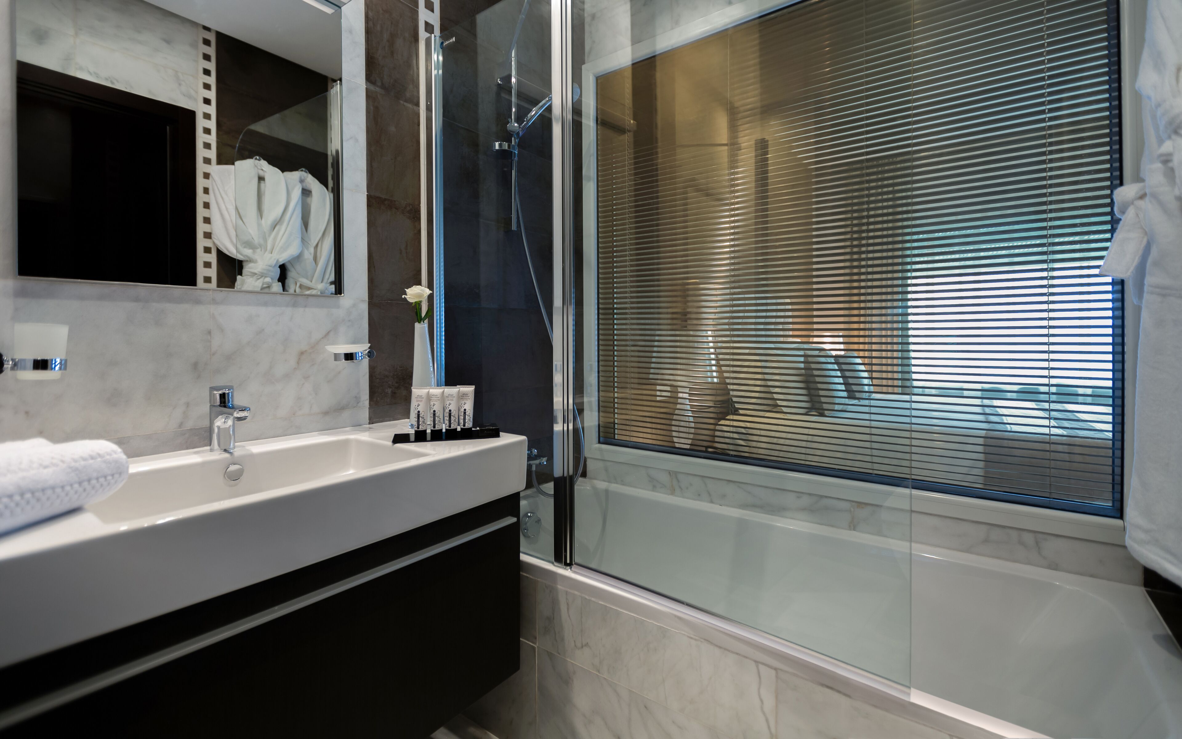 Un baño moderno con ducha acristalada, lavamanos de mármol y un espejo grande.