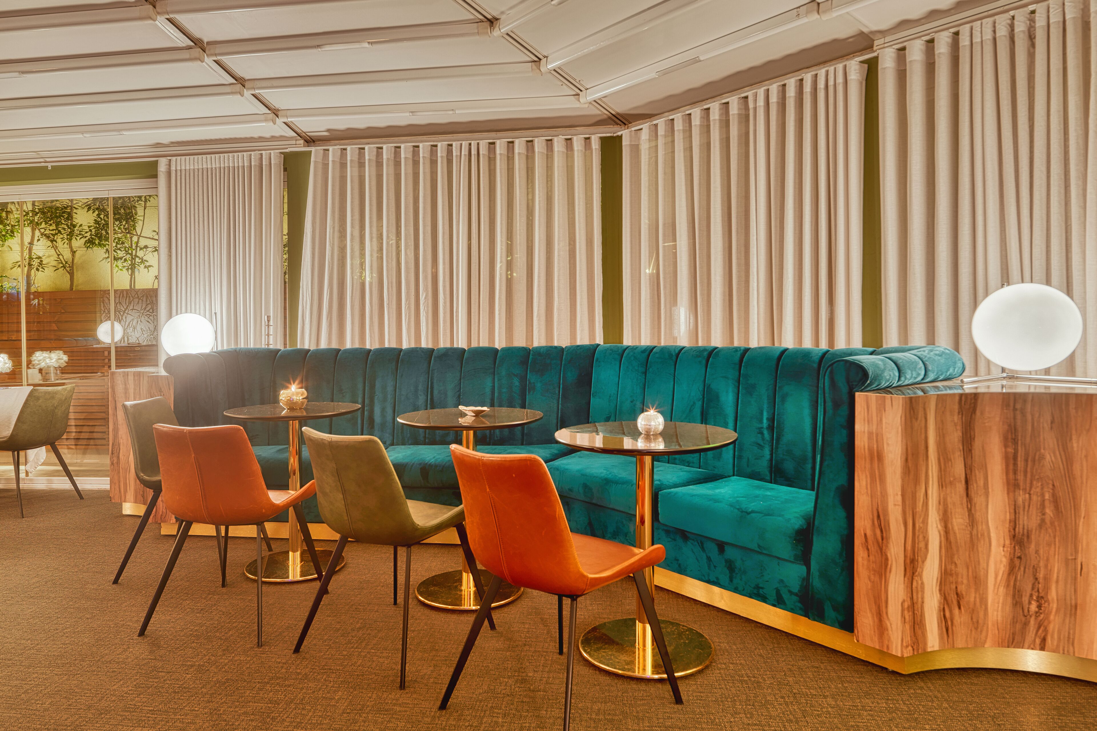 Et moderne loungeområde med en turkis sofa, orange og grønne stole samt en træreception.