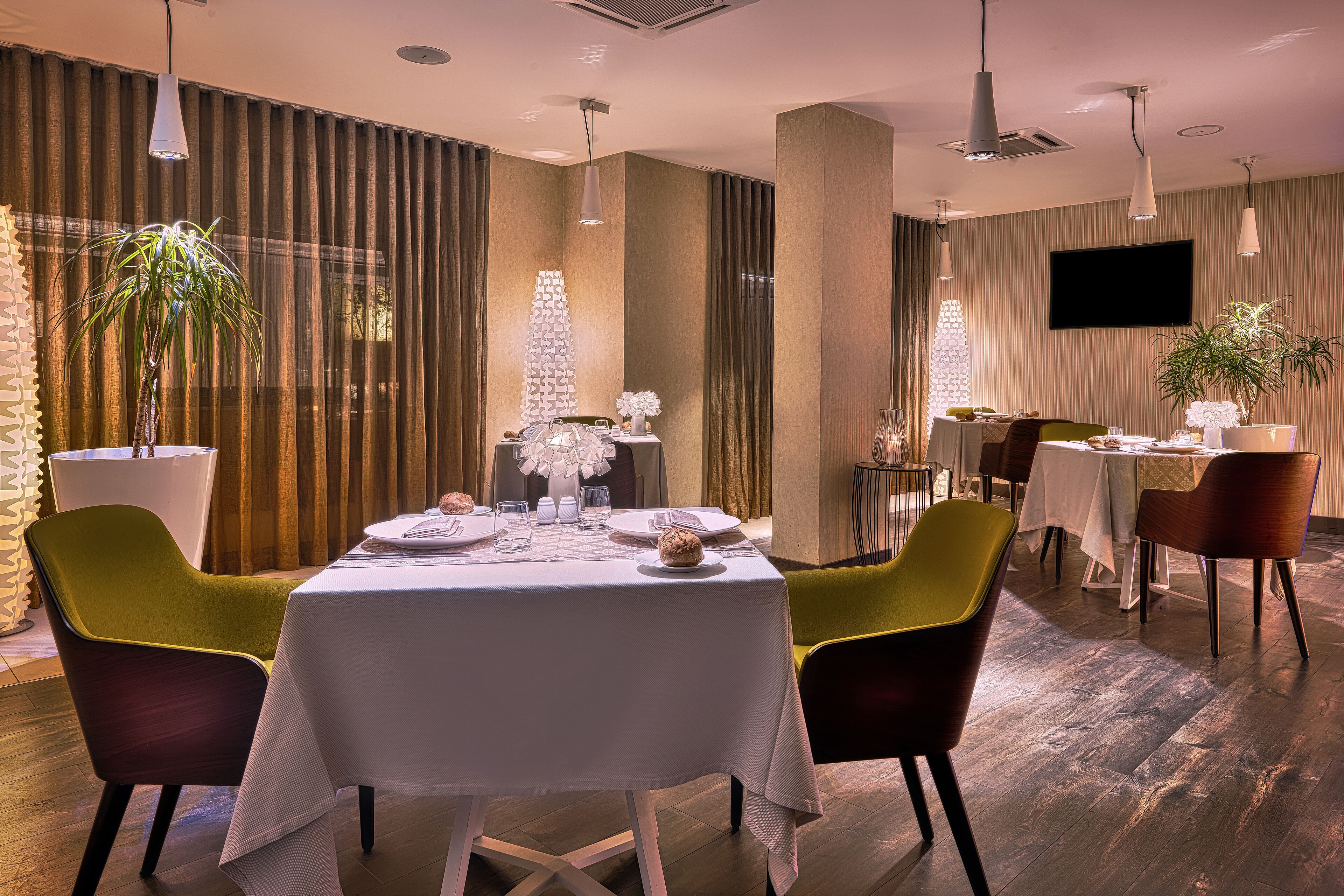 A modern dining area with a round table, green and brown chairs, and a potted plant.