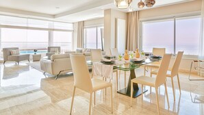 Amplia sala de estar con mesa de comedor de vidrio, sillas modernas y vista al océano.