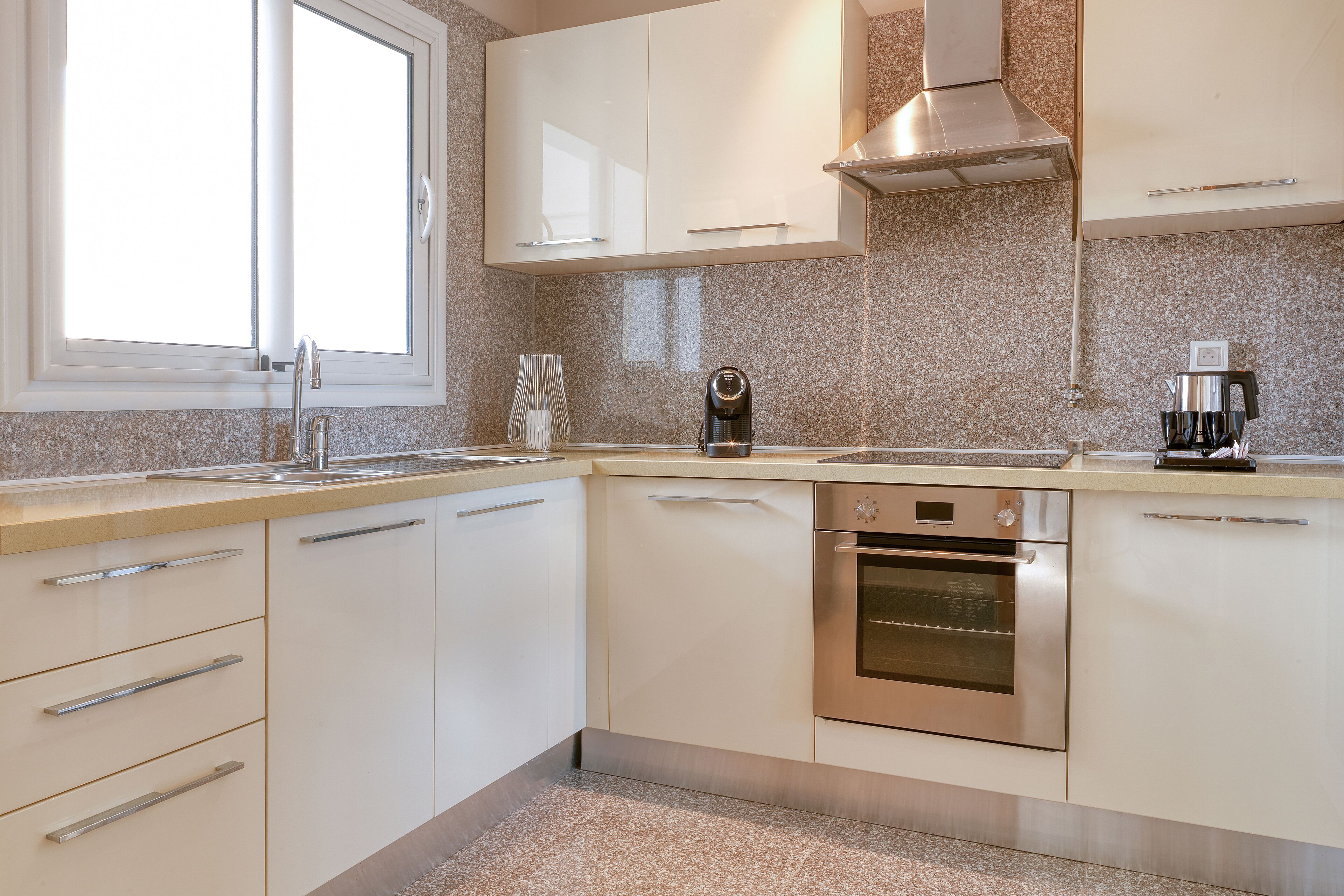 A modern kitchen with white cabinets, a stainless steel oven, and a window above the sink.