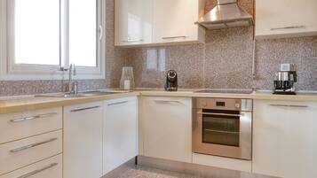 A modern kitchen with white cabinets, a stainless steel oven, and a window above the sink.