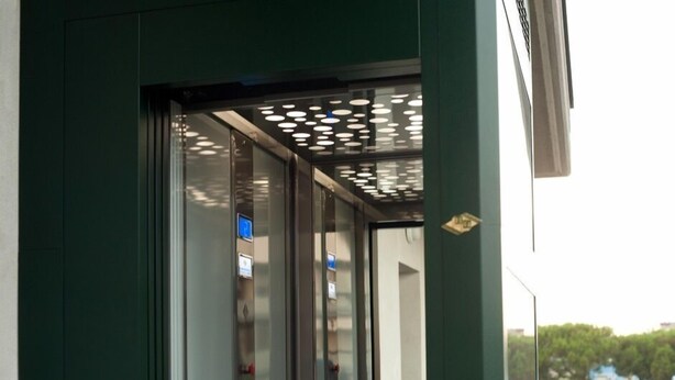 Vista interna de um elevador com design moderno, incluindo teto trabalhado e painel digital.