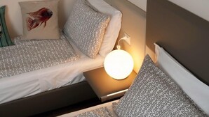 Cama bem arrumada com roupa de cama estampada, travesseiro decorativo com desenho de peixe e abajur.