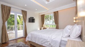 A bedroom with a large bed, a TV mounted on the wall, and a balcony with curtains. - Villa Kota Bunga Puncak 4 Bedroom (Cipanas)